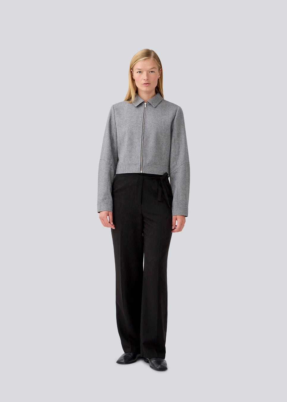 Cropped grey jacket in 80% wool. LissieMD jacket has a classic collar, manchet with button closure and a zipper in front. The model is 177 cm and wears a size S/36.