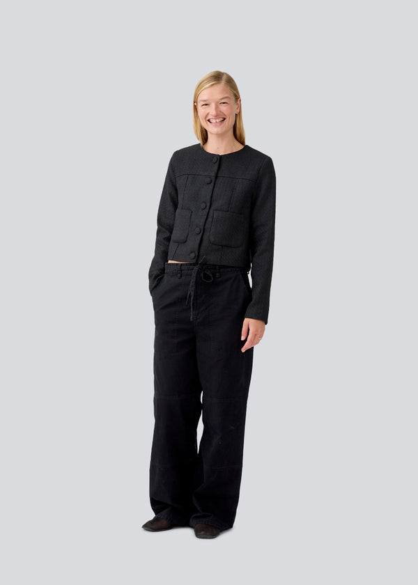 Short black jacket in a structured material. LuniMD jacket has two pockets in front and a button closure in front. The model is 177 cm and wears a size S/36.