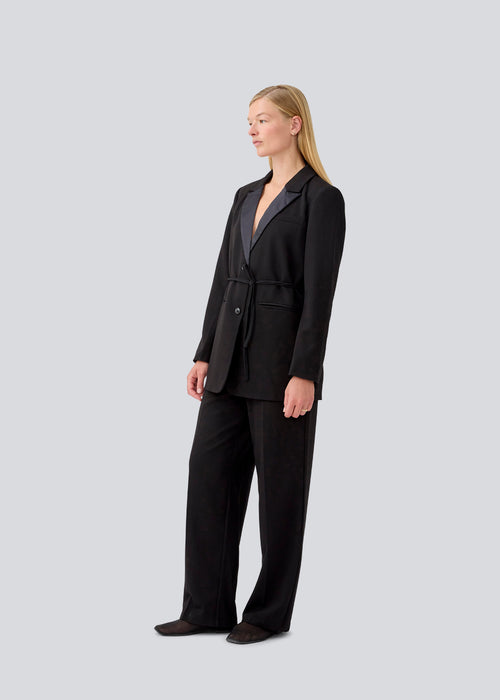 Classic black blazer with an oversize fit and a tieband at the waist. LykkeMD blazer has a satin detail on the collar and a slit in the back. The model is 177 cm and wears a size S/36.