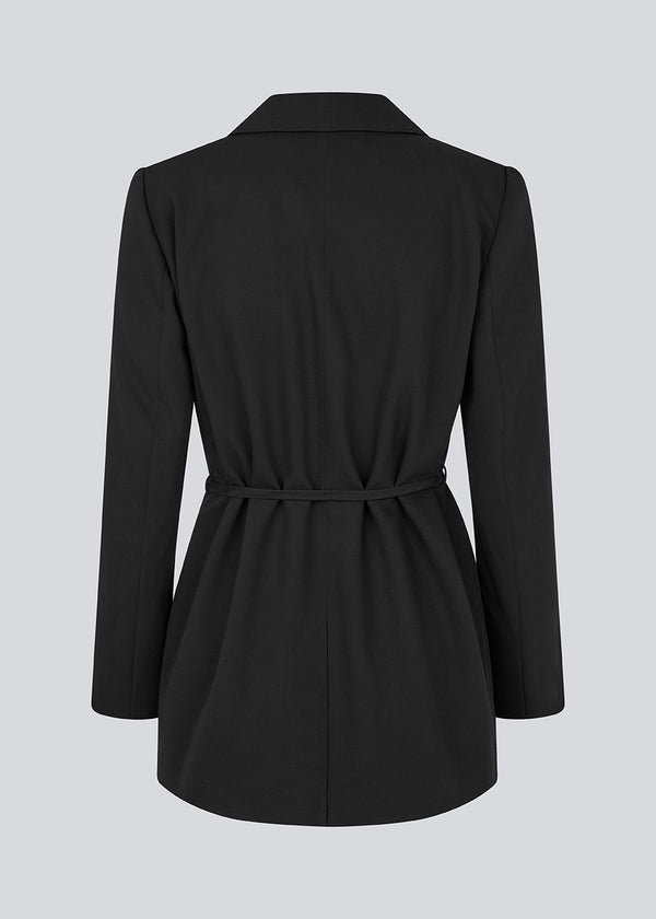 Classic black blazer with an oversize fit and a tieband at the waist. LykkeMD blazer has a satin detail on the collar and a slit in the back. The model is 177 cm and wears a size S/36.