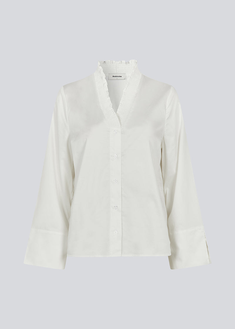 Lose white shirt with v-neck with a smock detail. LylaMD shirt has long wide sleeves with a slit and a buttonclosure in front.