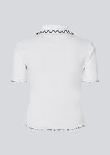 Fitted polo t-shirt in white with black edges in jersey. MagdaloneMD polo has short sleeves and babylock edges. The model is 177 cm and wears a size S/36