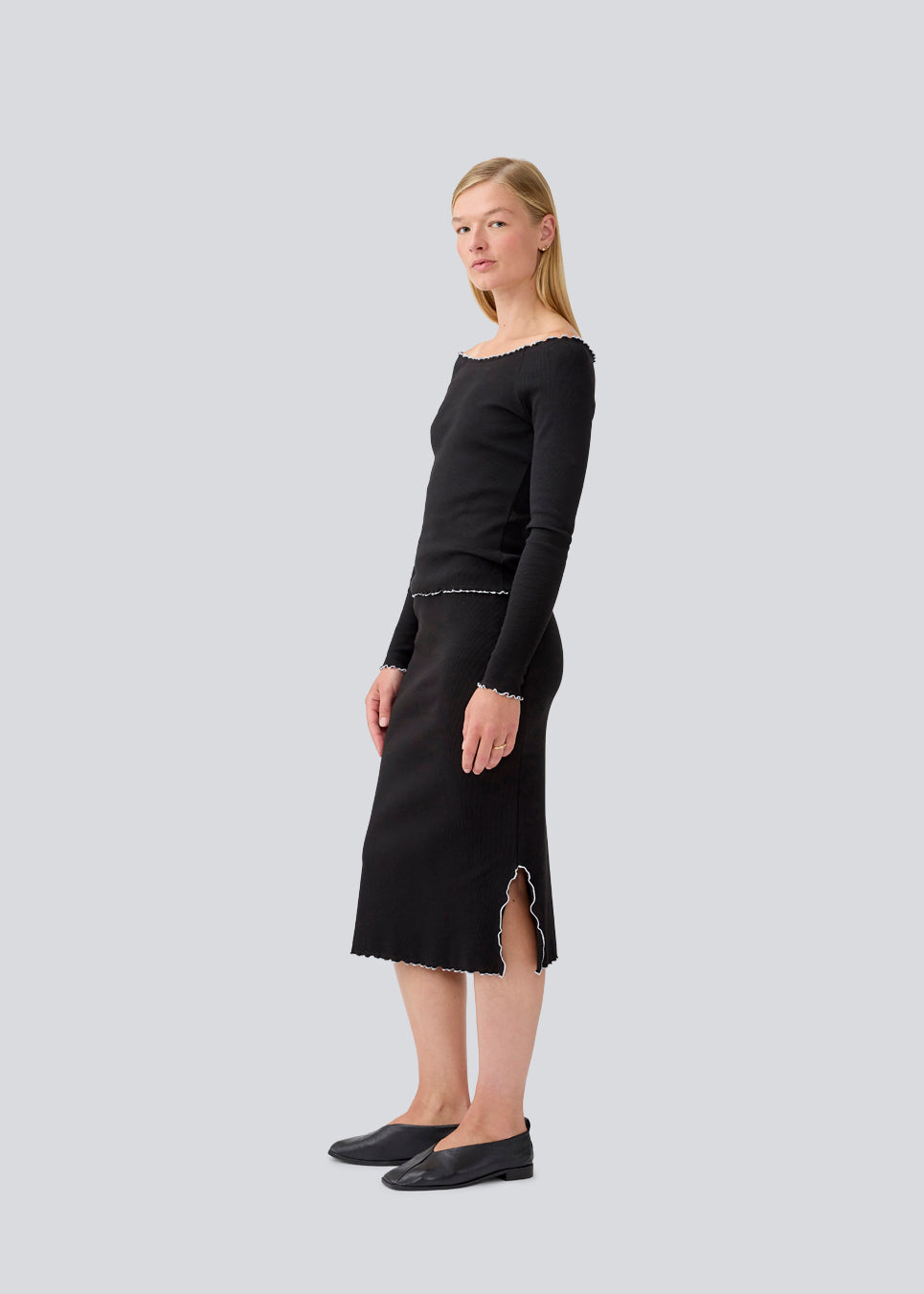 Midi skirt in black with white edges in jersey. MagdaloneMD skirt has slits in the sideseams and babylock edges with an elastic in the waist. The model is 177 cm and wears a size S/36.