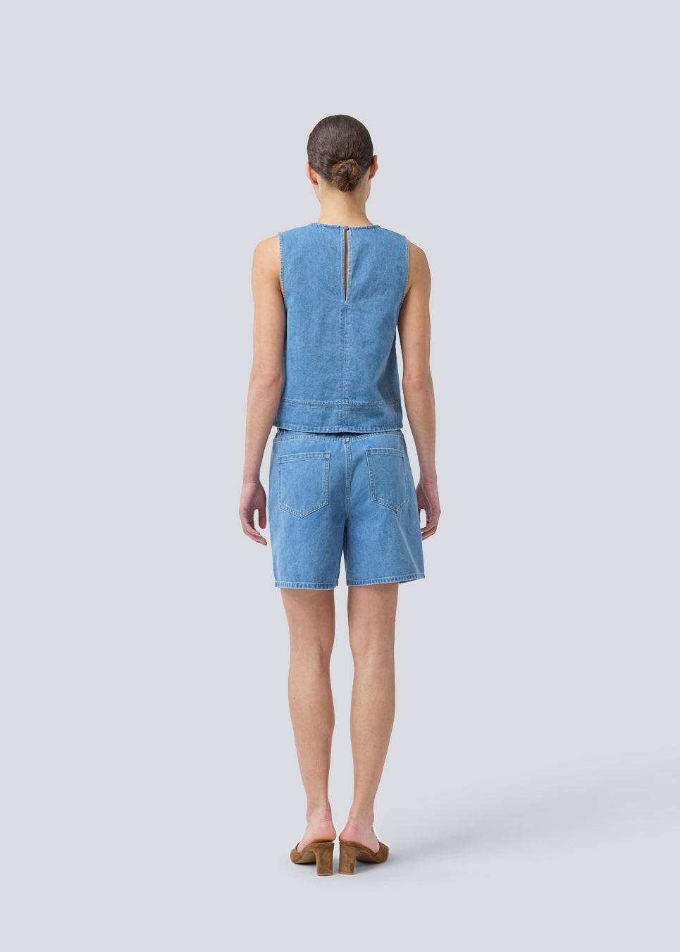 Sleeveless blue top with a round neck in cotton denim. NaomaMD solid top has a loose fit and an opening in the neck with a button closure.