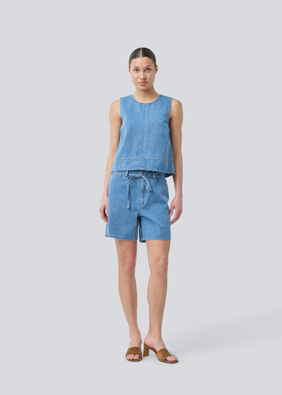 Sleeveless blue top with a round neck in cotton denim. NaomaMD solid top has a loose fit and an opening in the neck with a button closure.