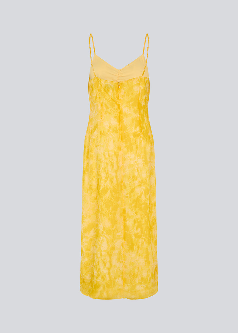 Maxi dress in yellow with thin straps and an elastic gathering at the chest. Napthalimd print strap dress has a slit in the front and an invisible zipper at the back.
