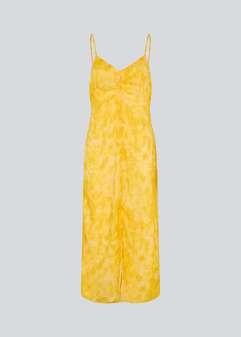 Maxi dress in yellow with thin straps and an elastic gathering at the chest. Napthalimd print strap dress has a slit in the front and an invisible zipper at the back.