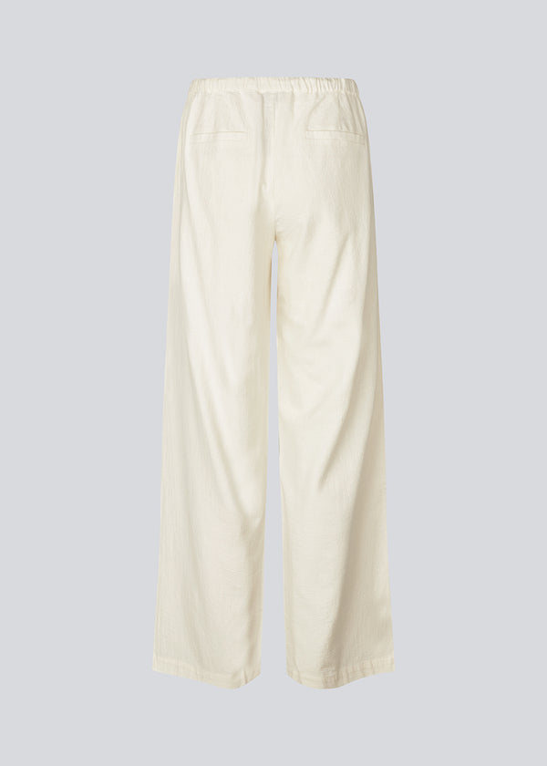 Loose white pants with wide legs made in 100% cotton. NasirMD pants have side pockets, an elastic waist with a string, and a stitched press fold at the front.