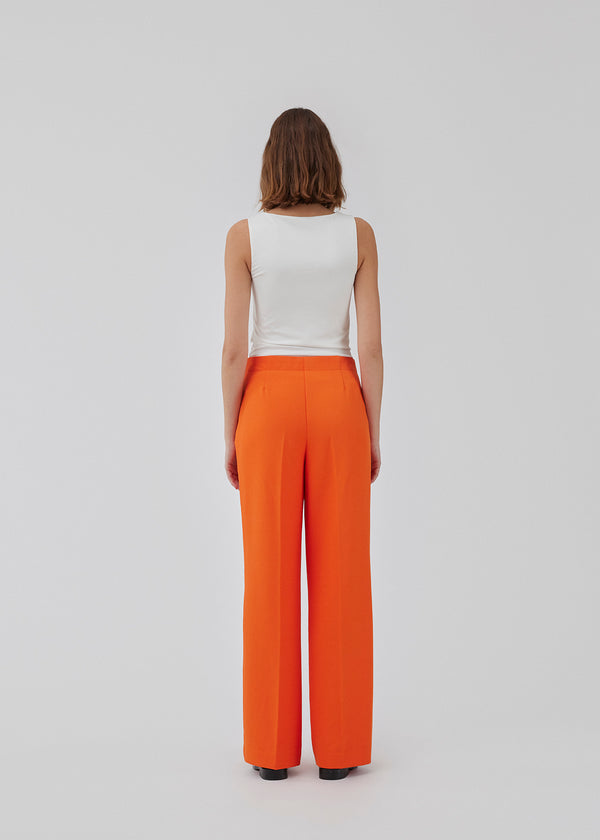 Classic pants in brigt red with pressfolds and straight legs. Nelli pants are closes by an hidden zipper at the side with an elastic waistband for a more comfortable fit. The model is 173 cm and wears a size S/36