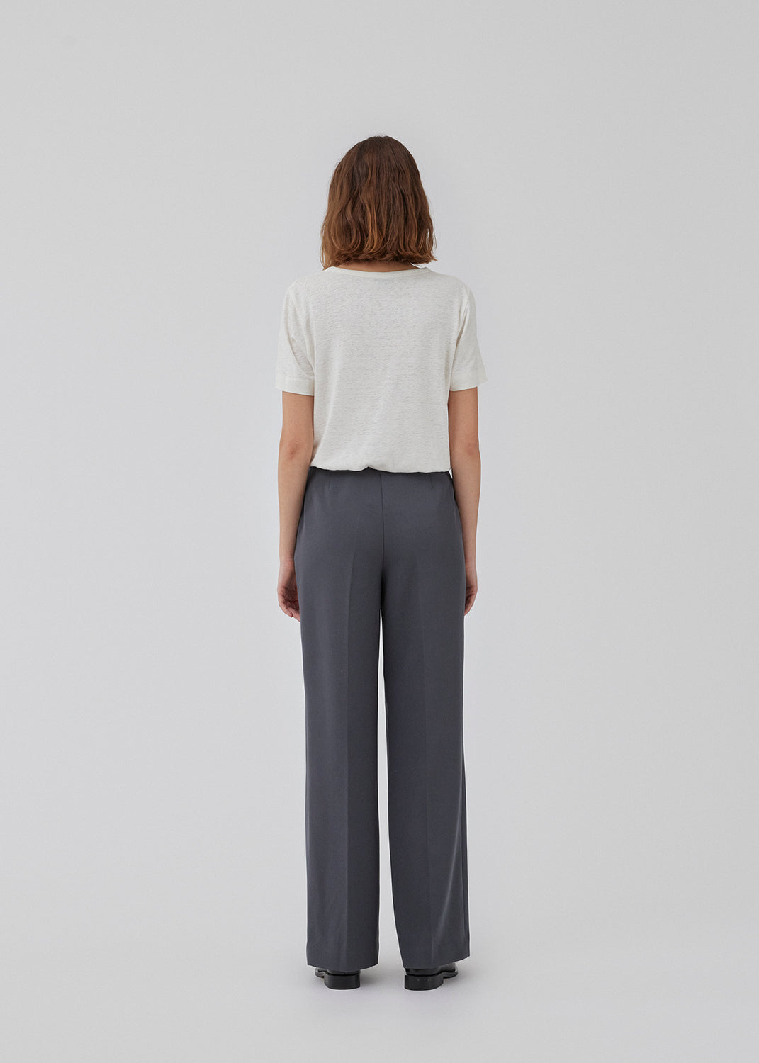 Classic pants in grey with pressfolds and straight legs. Nelli pants are closed by a hidden zipper at the side with an elastic waistband for a more comfortable fit. The model is 173 cm and wears a size S/36