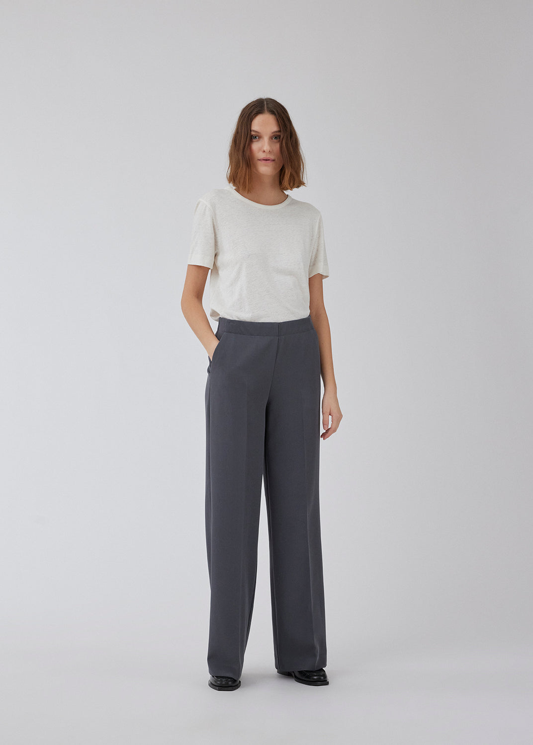 Classic pants in grey with pressfolds and straight legs. Nelli pants are closed by a hidden zipper at the side with an elastic waistband for a more comfortable fit. The model is 173 cm and wears a size S/36