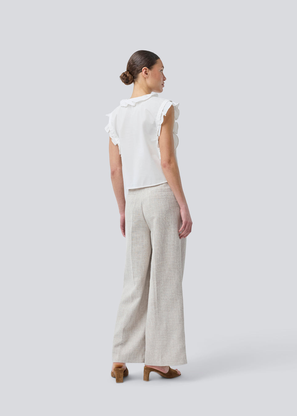 Sleeveless white top with frill details and a button closure in front. NIkkoMD top is slightly cropped and has a v-neck.