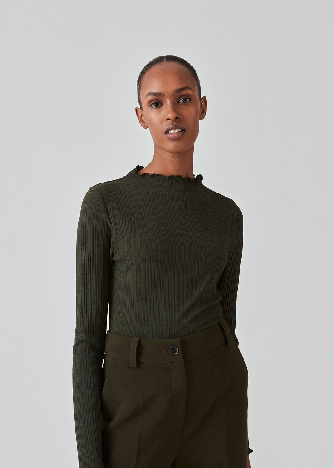 Tight-fitted, long sleeved t-shirt in dark green with ruffled trimmings on sleeves, at the neck and bottom. Oasis t-neck fits perfectly as a basic style in the wardrobe. The model is 173 cm and wears a size S/36