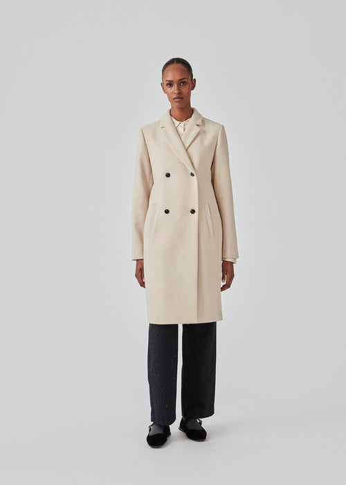 Beautiful, knee-length wool coat. Odelia coat, in season color Summer Sand, is closed at front by 4 buttons and is fitted around the waist, which gives a feminine look. Because of the high content of wool the jacket will be perfect for fall and the mild winters.