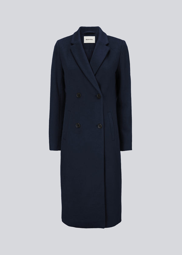 Beautiful, long woolen coat in navy blue. Odelia long coat is double-breasted and slightly fitted at the waist for a feminine expression. The coat is an obvious choice for both fall and mild winters.