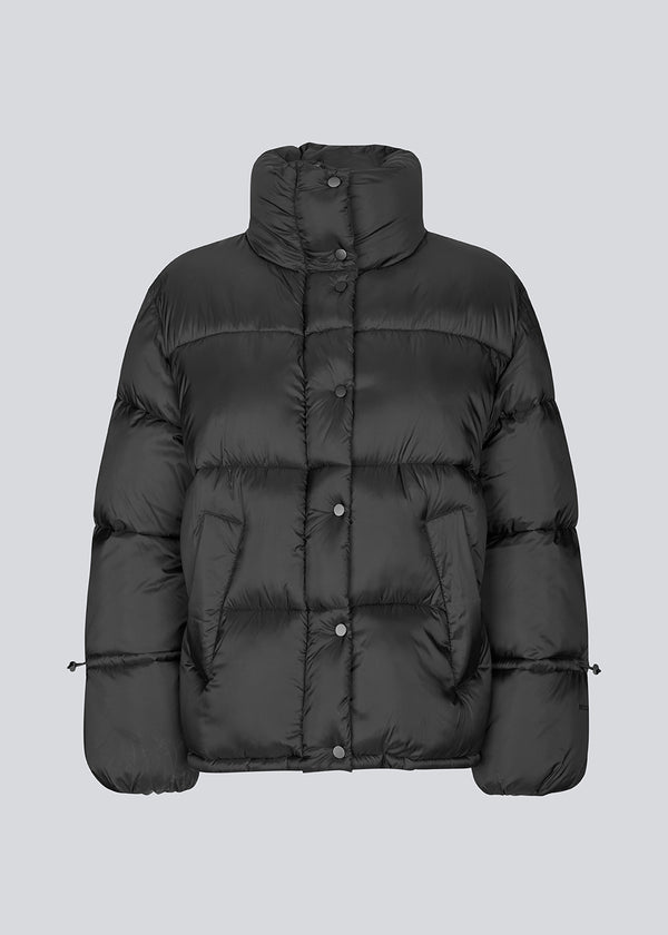 Black puffer jacket with a high neck in 100% recycled polyester. Odinmd jacket has a zipper closure and an adjustable strap at the sleeve. The model is 175 cm and wears a size s/36.