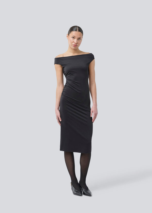 Long off-shoulder dress in elastic recycled material. Parissamd dress is fitted and has ruffle details at the sides. The model is 175 cm and wears a size S/36.