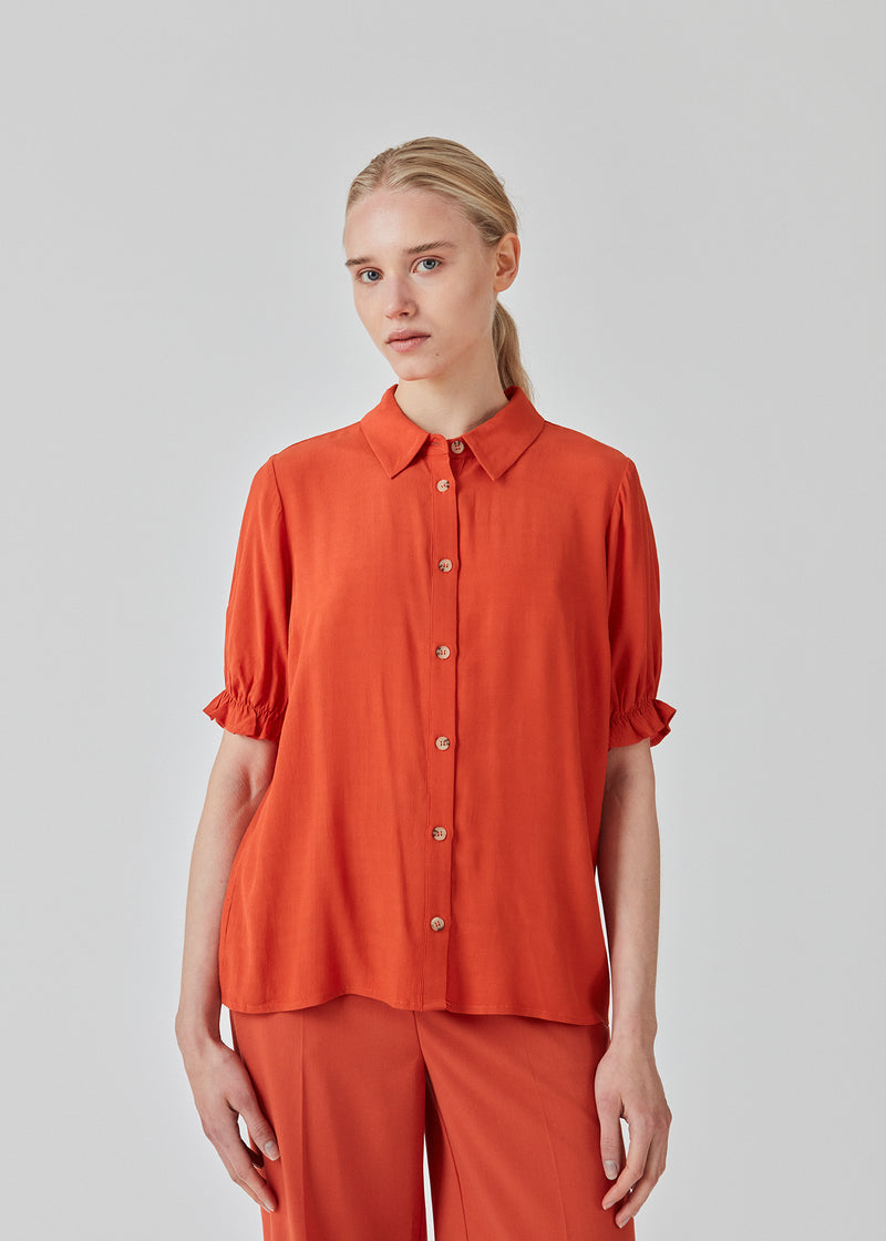 Red shirt with short puff sleeves with elasticated trim. RavenMD print shirt has a normal collar and buttons on front. The fit is relaxed. The model is 173 cm and wears a size S/36