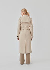 Classic, double-breasted wool coat in beige with collar and notch lapels. ShayMD coat has a wide tiebelt at waist, shoulder straps, wide cuffs and open yoke. With lining and single back vent.