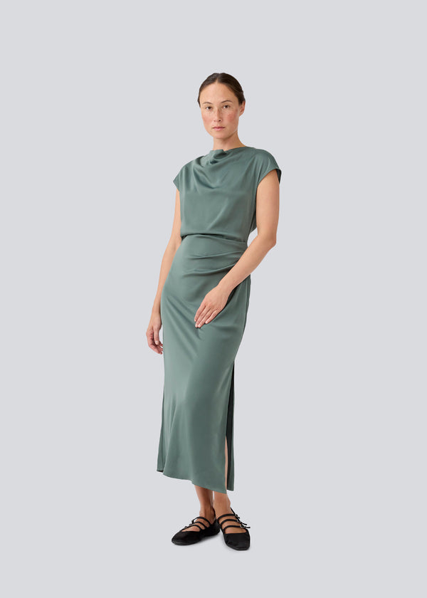 Sleeveless maxi dress in beautiful green with pleats on the side. TailorMD dress is made in satin and has a high neck, an invisible zipper in the back, and a slit in the side seam. The model is 177 cm and wears a size s/36.
