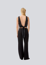 Sleeveless black top in satin. TailorMD top has an open back with a tieband. The model is 177 cm and wears a size S/36.
