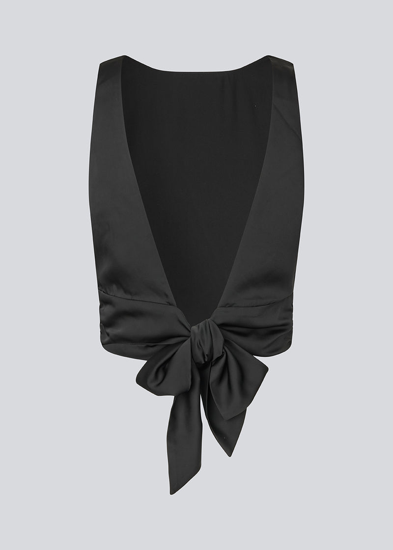 Sleeveless black top in satin. TailorMD top has an open back with a tieband. The model is 177 cm and wears a size S/36.