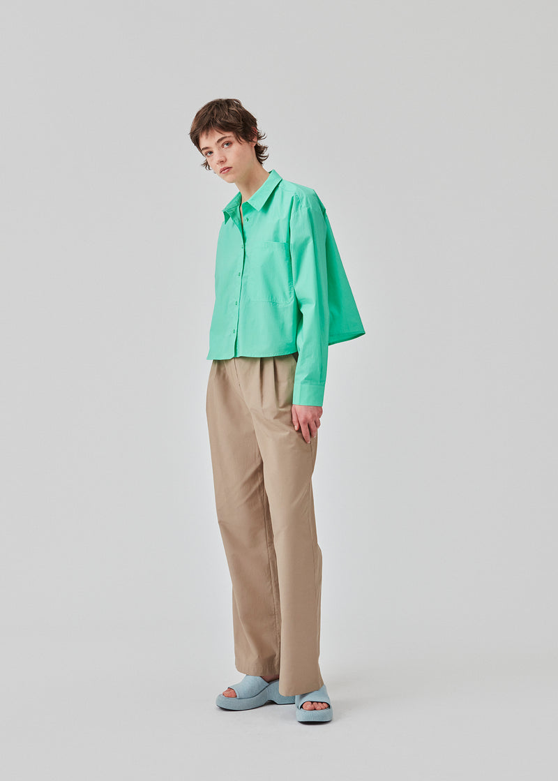 Airy shirt in the color Calm Jade in organic cotton poplin. TapirMD shirt has a collar and buttons in front, with an open chest pocket. Dropped shoulders and long sleeves with cuff and button. Embroidered logo in front.
