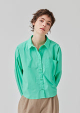 Airy shirt in the color Calm Jade in organic cotton poplin. TapirMD shirt has a collar and buttons in front, with an open chest pocket. Dropped shoulders and long sleeves with cuff and button. Embroidered logo in front.
