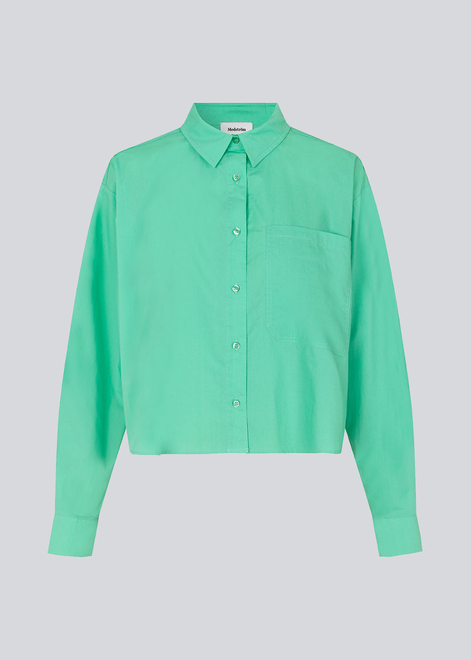Airy shirt in the color Calm Jade in organic cotton poplin. TapirMD shirt has a collar and buttons in front, with an open chest pocket. Dropped shoulders and long sleeves with cuff and button. Embroidered logo in front.