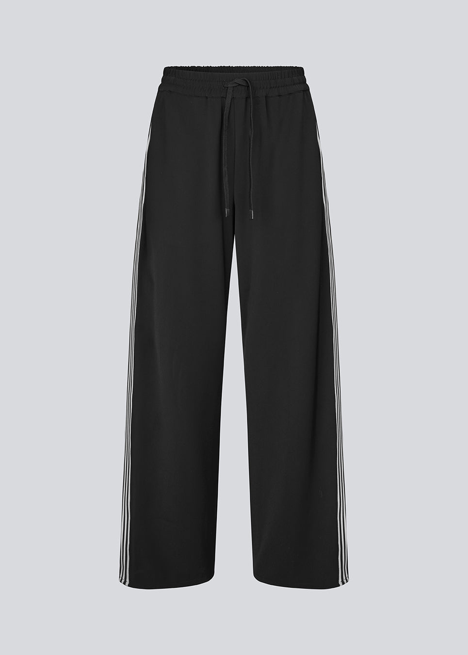 Loose black trousers with wide legs and a relaxed fit. Featuring an elastic waistband with drawstring for a comfortable, adjustable waist. White side stripes add a sporty and modern touch to the otherwise classic design. Perfect for casual everyday wear or more elevated styling – easy to pair with everything from t-shirts to dressy tops.
