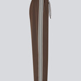 Loose brown trousers with wide legs and a relaxed fit. Featuring an elastic waistband with drawstring for a comfortable, adjustable waist. White side stripes add a sporty and modern touch to the otherwise classic design. Perfect for casual everyday wear or more elevated styling – easy to pair with everything from t-shirts to dressy tops.