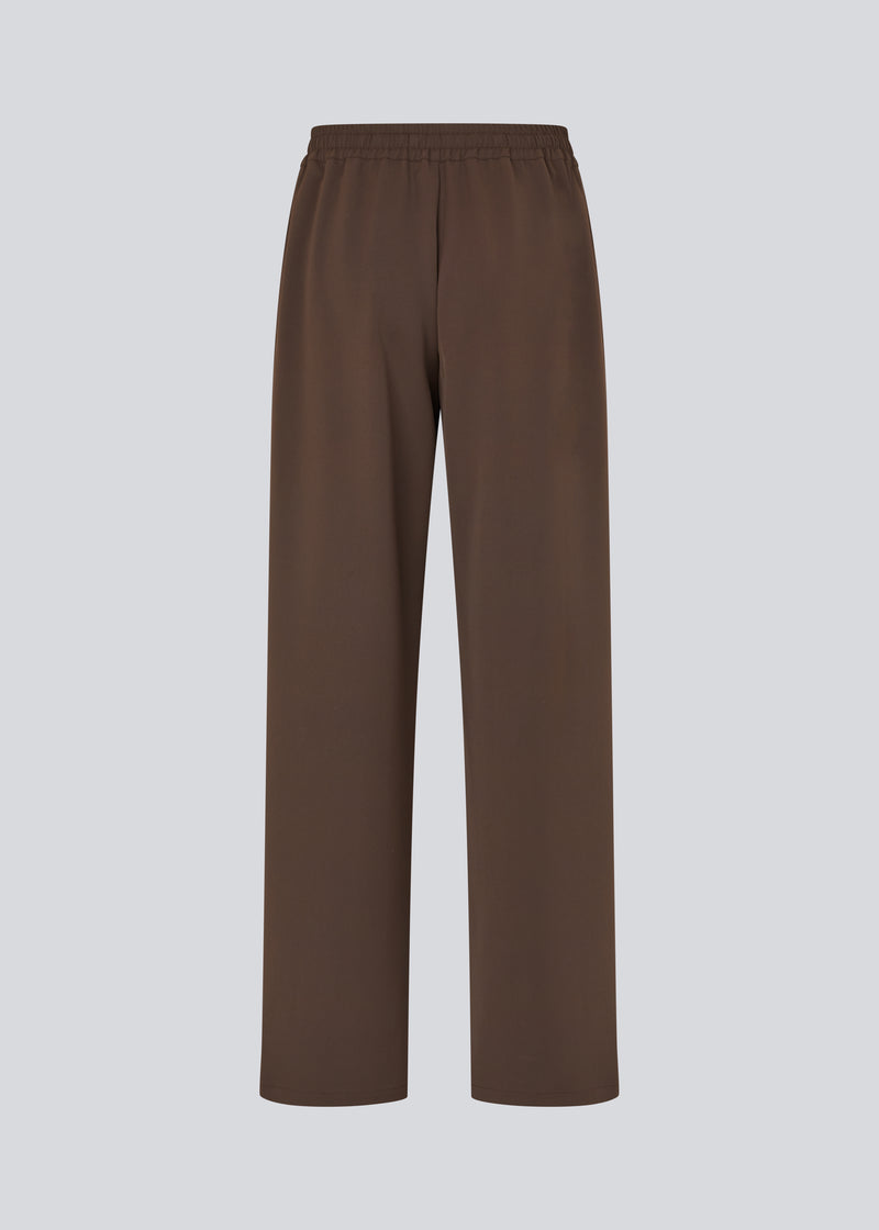 Loose brown trousers with wide legs and a relaxed fit. Featuring an elastic waistband with drawstring for a comfortable, adjustable waist. White side stripes add a sporty and modern touch to the otherwise classic design. Perfect for casual everyday wear or more elevated styling – easy to pair with everything from t-shirts to dressy tops.