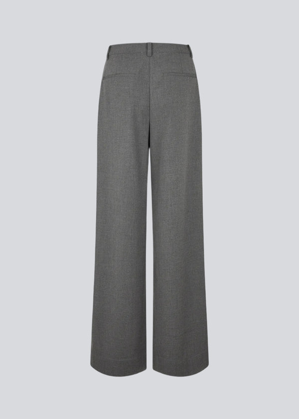 Grey suit pants with pleats and wide legs. Tuesdaymd pants have a medium-highwaist, zipper, side pockets and paspoil pockets in the back. The model is 175 cm and wears a size s/36.