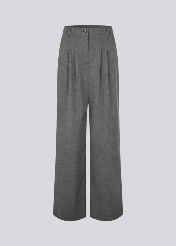 Grey suit pants with pleats and wide legs. Tuesdaymd pants have a medium-highwaist, zipper, side pockets and paspoil pockets in the back. The model is 175 cm and wears a size s/36.