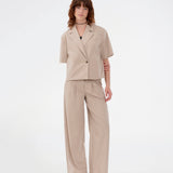 Suit pants in beige with pleats and wide leg. Tuesdaymd pants have a medium-highwaist, zipper, side pockets and paspoil pockets in the back. The model is 175 cm and wears a size s/36.