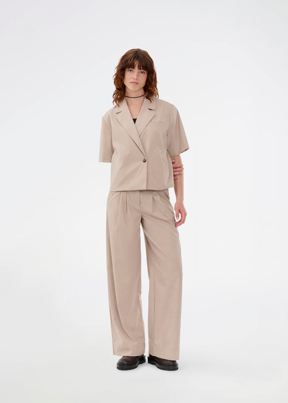 Suit pants in beige with pleats and wide leg. Tuesdaymd pants have a medium-highwaist, zipper, side pockets and paspoil pockets in the back. The model is 175 cm and wears a size s/36.