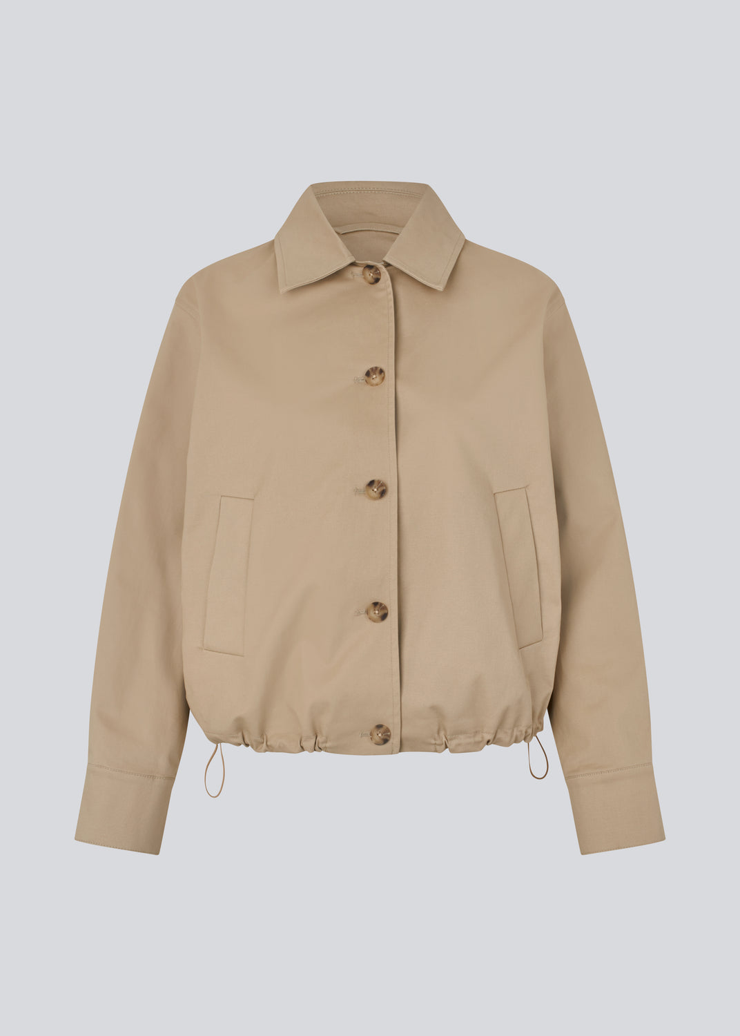 Short jacket i beige with a trench coat look. The Umamd jacket features a shirt collar, side pockets, button closure, and an adjustable elastic hem. The model is 175 cm and wears a size S/36.

Material:
97% Cotton
3% Elastane

Lining:
100% Polyester