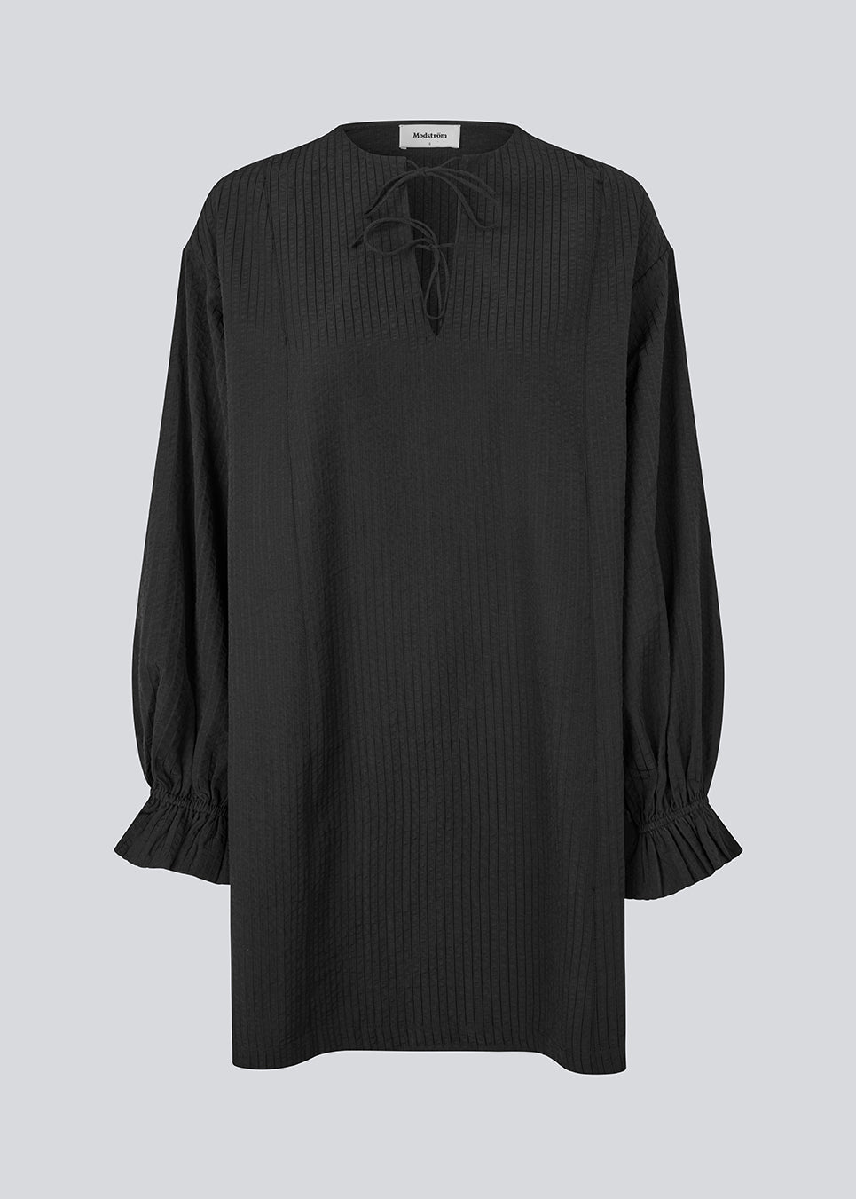 Elegant black dress in a lightweight textured fabric. The UrsaMD Dress features a relaxed, straight fit with long, voluminous sleeves and feminine ruffle details at the wrists. The round neckline has a small V-cut with tie strings, adding a delicate and relaxed touch.

Material:
40% Cotton
60% Recycled Polyester
