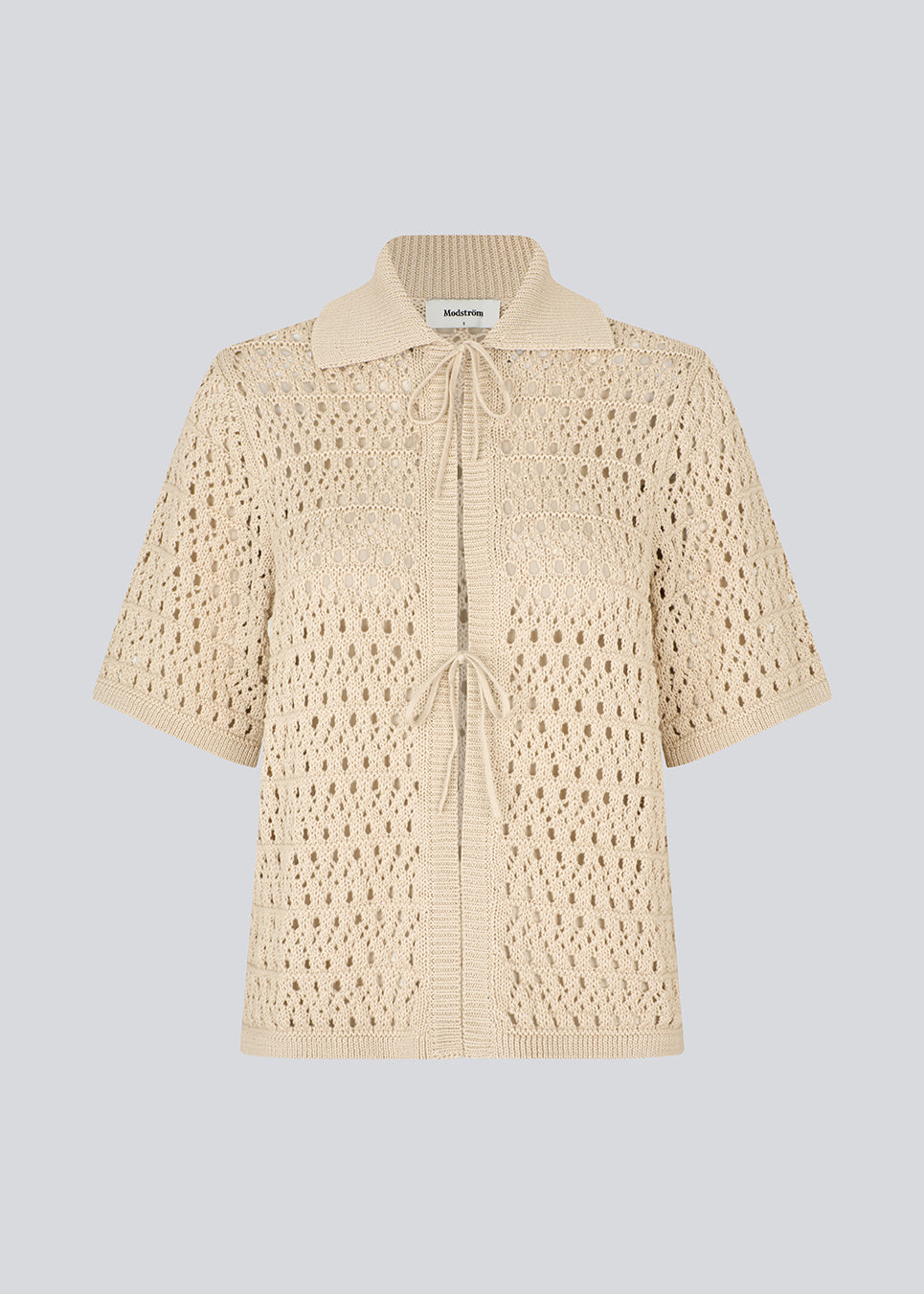 Elegant and lightweight cardigan in beige in a beautifully knitted openwork pattern. The VesterMD cardigan features short sleeves, a collar, and an adjustable drawstring closure at the front, creating a feminine and relaxed look. Made from 100% organic cotton for soft and breathable comfort.