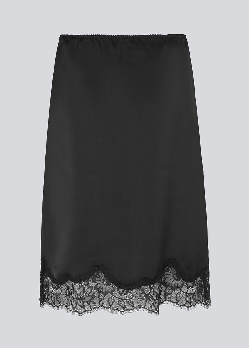 Black satin skirt with lace hem on a light gray background