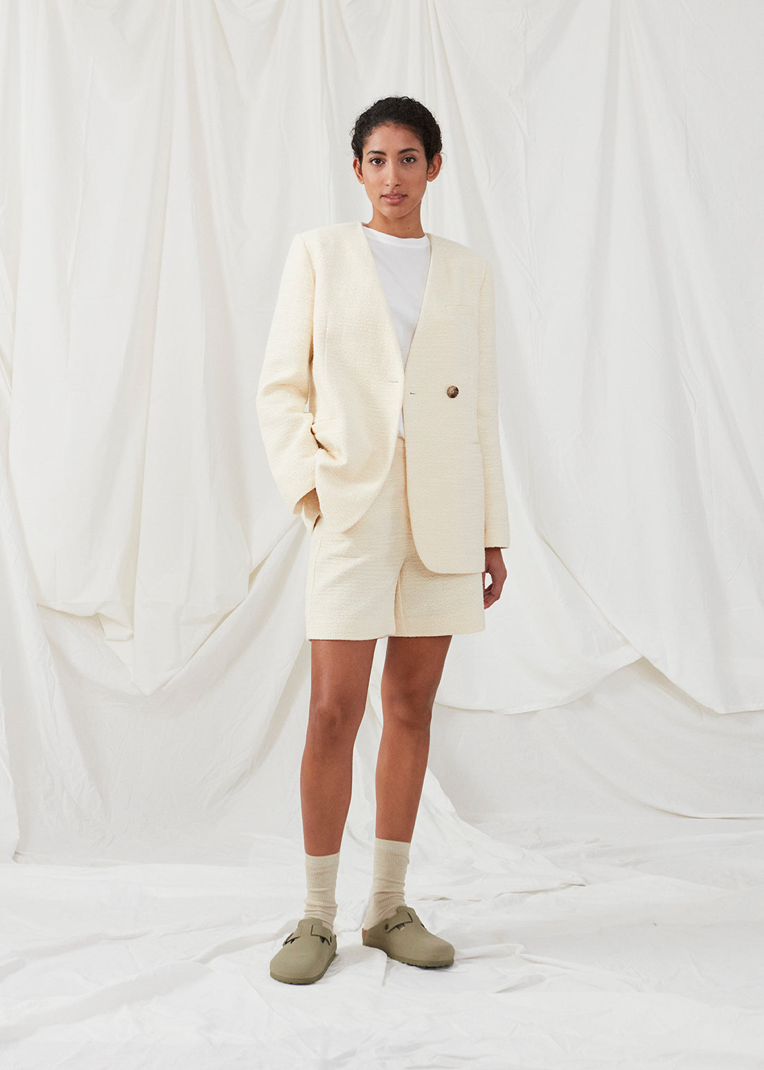 DimeMD blazer is designed in a textured cotton blend with lining. The blazer is collarless but has an asymmetrical wrap detail with a single visible button. The model is 177 cm and wears a size S/36.  Style the blazer with matching shorts: DimeMD shorts.