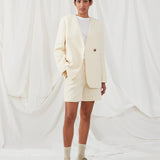 DimeMD blazer is designed in a textured cotton blend with lining. The blazer is collarless but has an asymmetrical wrap detail with a single visible button. The model is 177 cm and wears a size S/36.  Style the blazer with matching shorts: DimeMD shorts.