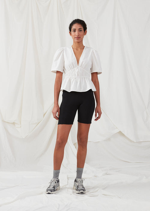 White top made from a cotton mix with short, slightly puffed, sleeves, and a deep v-neckline. DeenMD top has a flattering ruched detail below the chest and at the waist. The model is 177 cm and wears a size S/36.