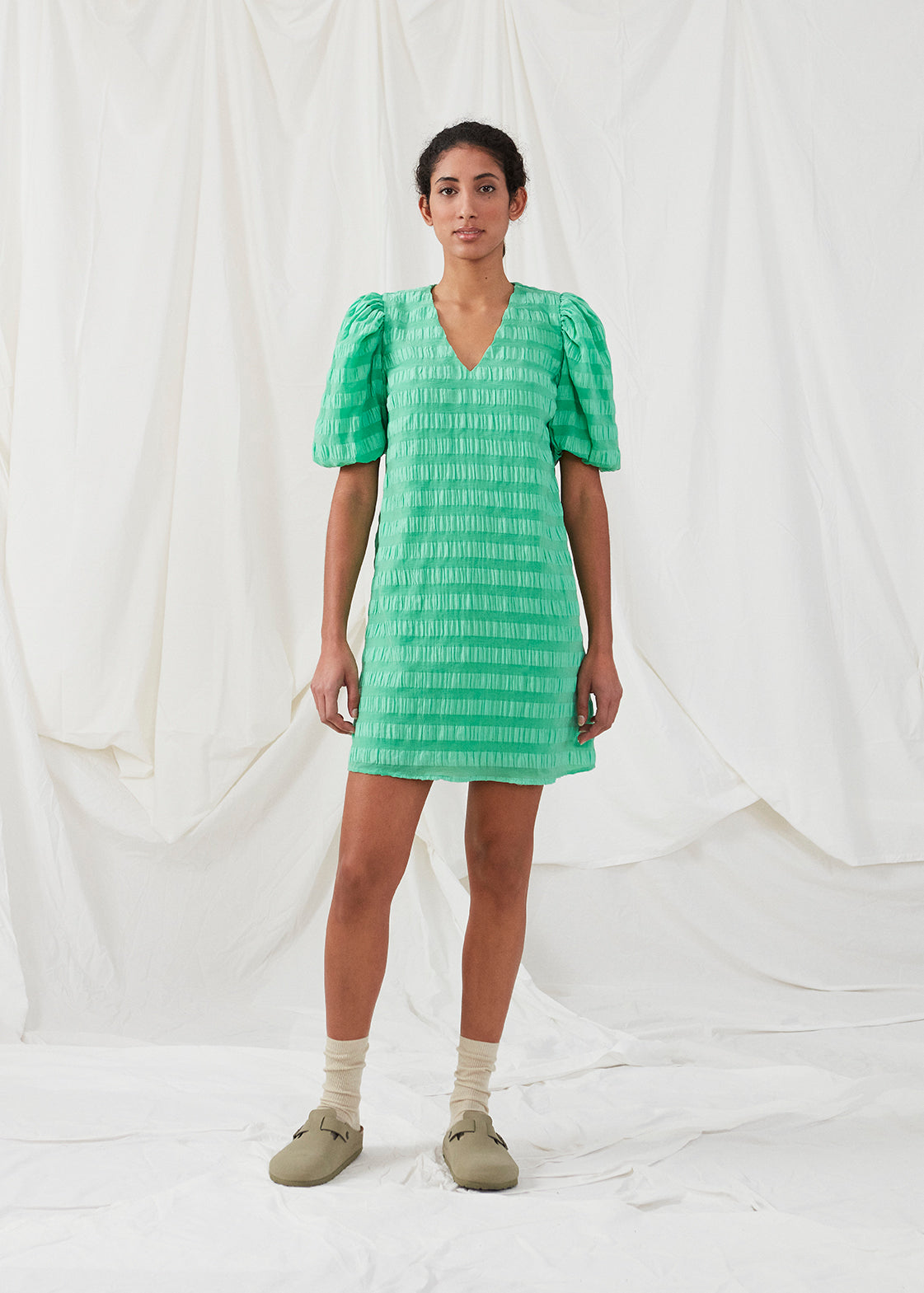 Short dress in green in a seersucker material. DinoMD dress has a v-shaped neckline, a loose silhouette, and short puff sleeves with elastic. The model is 177 cm and wears a size S/36.