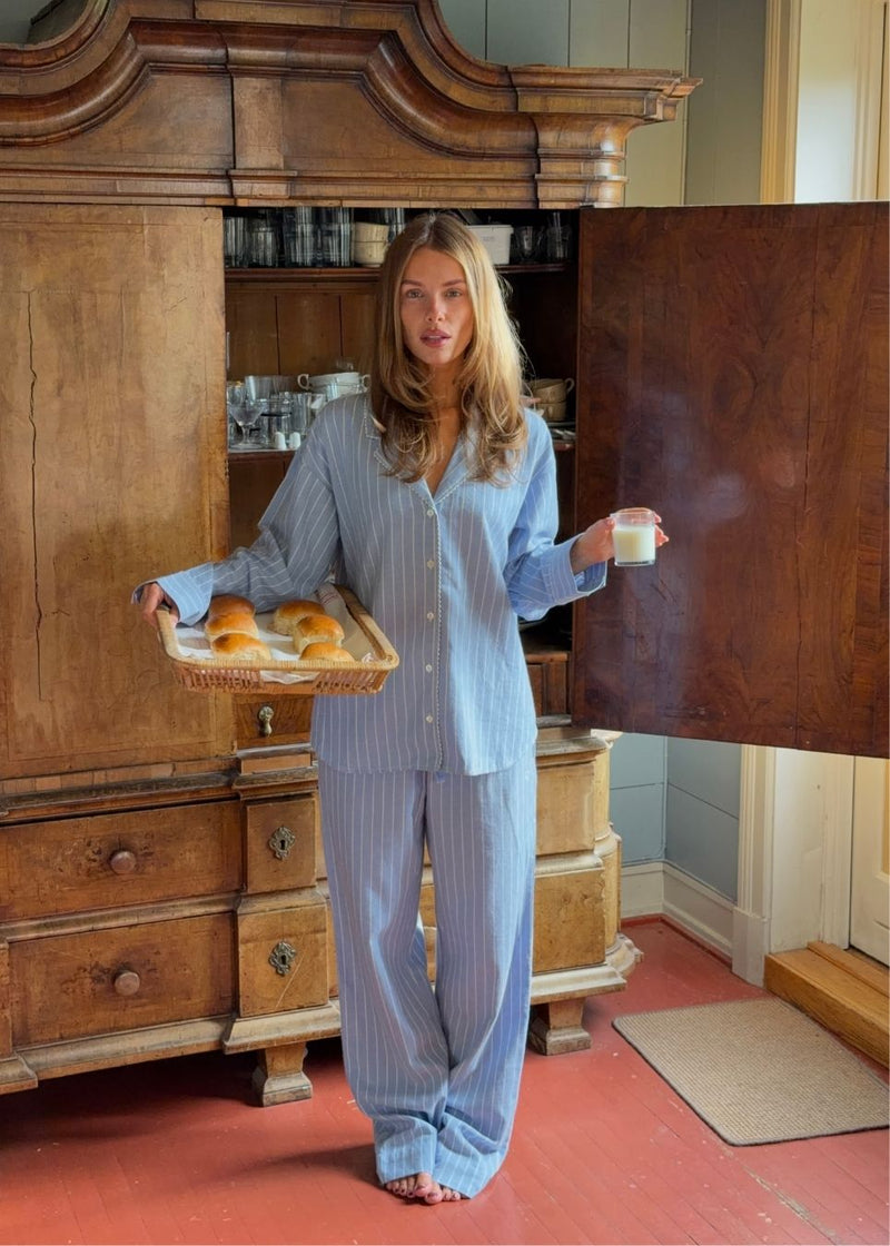 Blue classic striped pyjamas. The pyjamas is sold as a set of shirt and pants in the same size. Josefinemd pyjamas are made from 100% soft cotton and feature a classic fit with a collar, button closure, and drawstring trousers. Finished with delicate wave trim and comes with a matching pouch with logo. Josefine Vogt (165 cm) and the model (177 cm) are both wearing size Small.