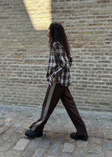 Loose brown trousers with wide legs and a relaxed fit. Featuring an elastic waistband with drawstring for a comfortable, adjustable waist. White side stripes add a sporty and modern touch to the otherwise classic design. Perfect for casual everyday wear or more elevated styling – easy to pair with everything from t-shirts to dressy tops.