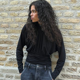 Elegant black blouse featuring a high neckline and long sleeves. Designed with delicate gathered details at the bust and waist to create a flattering silhouette. A subtle button closure at the back of the neck adds a refined and feminine touch. The stretchy fabric ensures a comfortable fit, while the draped design offers timeless elegance. Perfect for both everyday wear and special occasions.