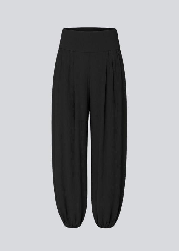 Balloon pants in black with a relaxed fit, made from 100% recycled polyester. Tullemd pants have an invisible side zipper, side pockets, and elastic at the leg hems.