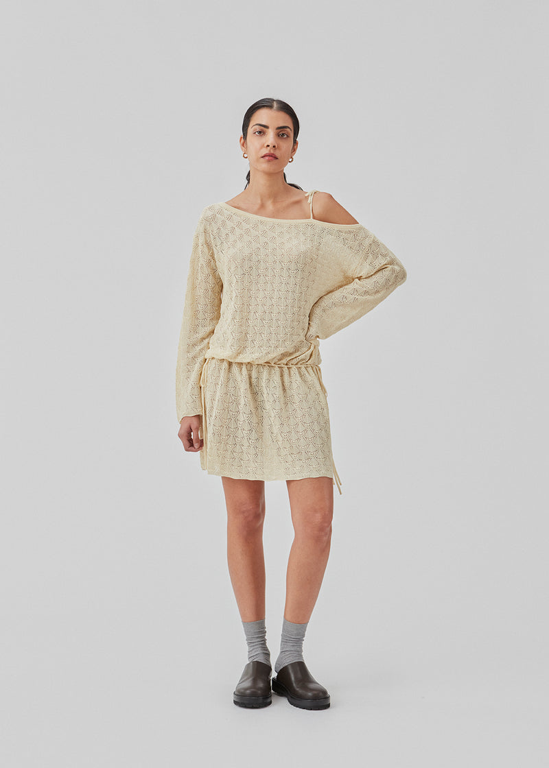 Loose-fit knitted dress with a pointelle pattern. JosefineMD knit dress has asymmetrical sleeves with ties over one shoulder and adjustable ties at the waist. The model is 177 cm and wears a size S/36.