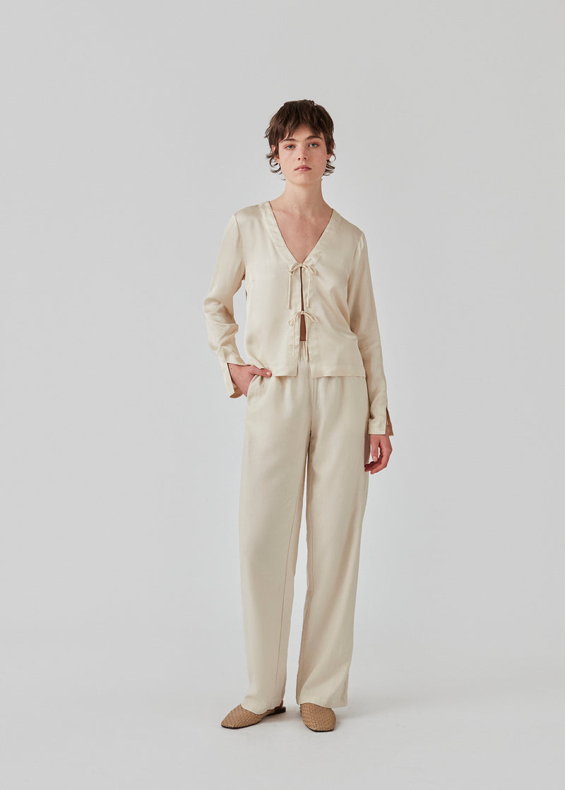 TulaMD shirt in an EcoVero viscose. The shirt is designed with a v-shape at the neckline, an opening in front with tie, and long sleeves with a slit. The model is 177 cm and wears a size S/36.  Material: 45% Viscose 55% Eco Vero Viscose